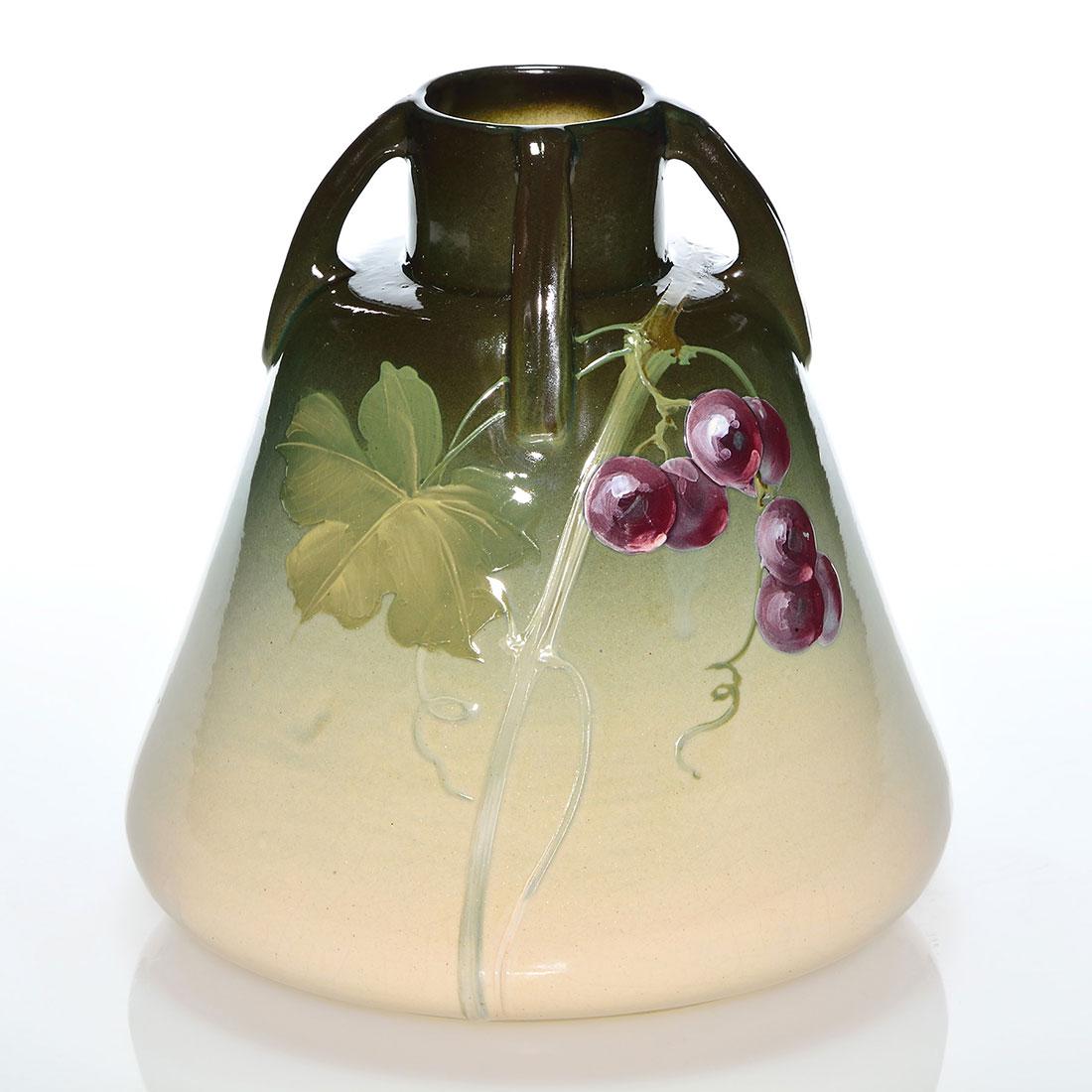 Weller Eocean Rose vase, grapes, Mitchell, 7 5/8”: Weller Eocean Rose four handled vase with grapes decoration painted by Lillie Mitchell who lightly incised her name beneath one handle. Incised Weller Eocean Rose and impressed 9013 on the bottom. The
