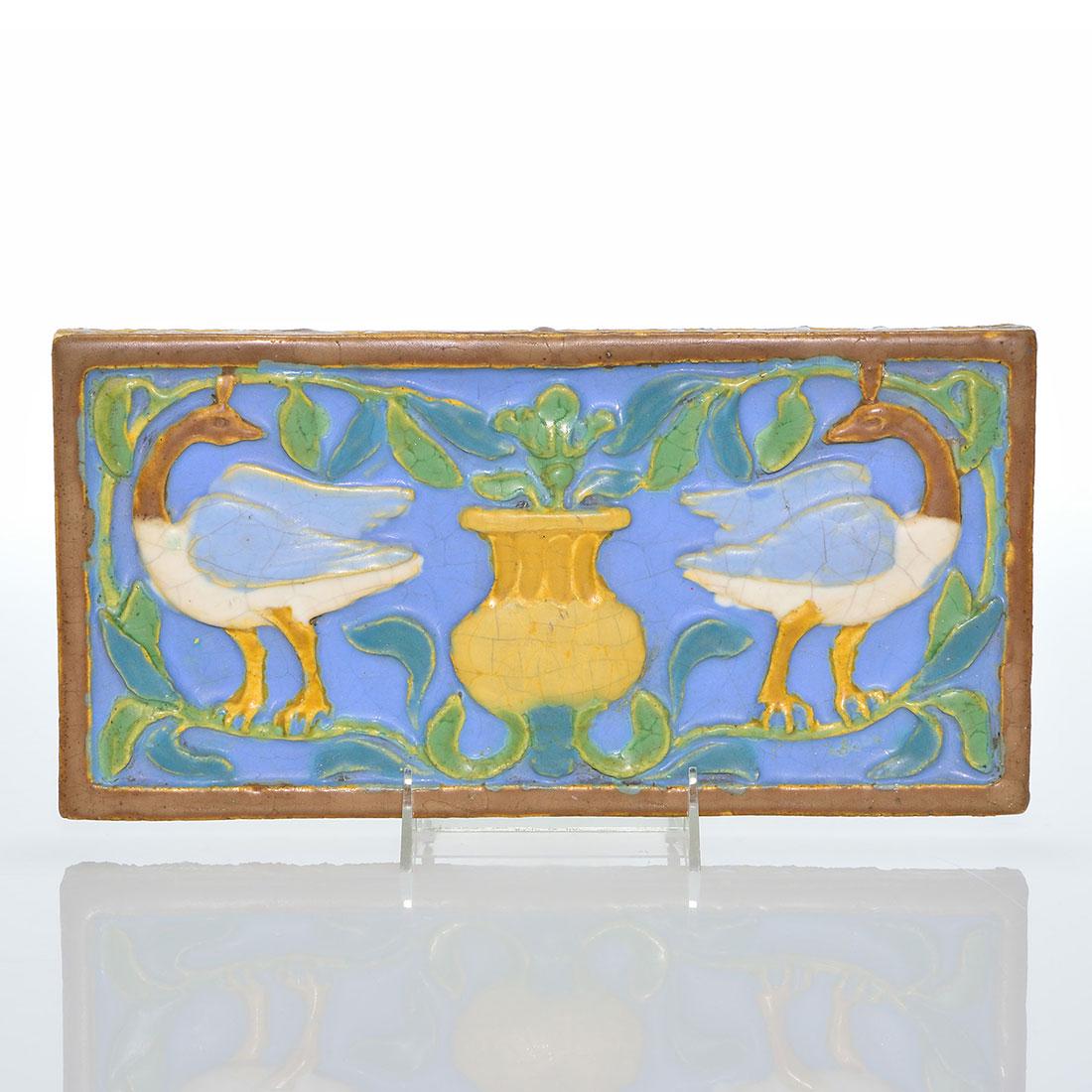 Wheatley Architectural tile birds, flowers, 6 3/8”: Architectural tile that we believe to be Wheatley featuring two blue winged geese standing on either side of a wildly flowering vase. Done in thick mat glazes, the tile is unmarked save for an incised