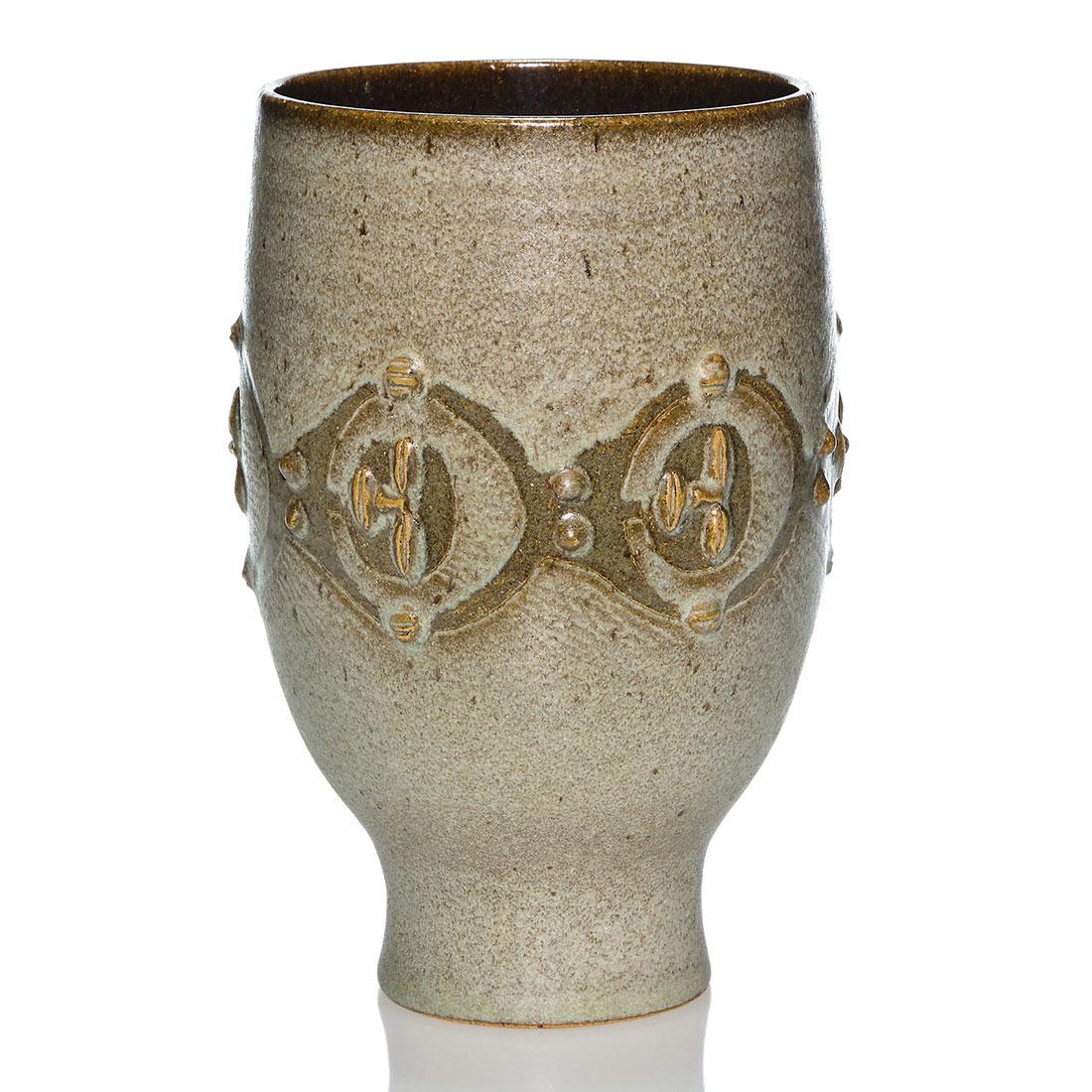 Edwin and Mary Scheier vase with faces, 10 1/4”,: Edwin and Mary Scheier vase with a band of carved faces that appear to be covered with football helmets, done in a speckled gray glaze over walnut brown. Measures 10 1/4 inches by 6 1/4 inches across