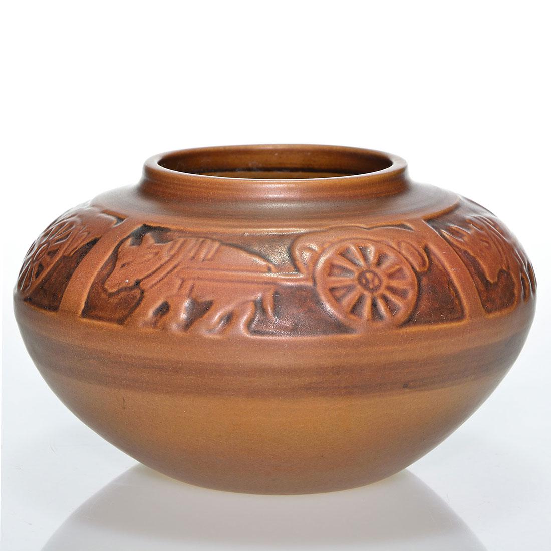 UND Ox Cart vase, 3 7/8” x 6 3/4”, Cable: UND shouldered vase with oxen pulling a cart within four panels based on a Flora Huckfield design and covered in light and dark brown glazes. Measures 3 7/8 inches by 6 3/4 inches across. Incised Red 