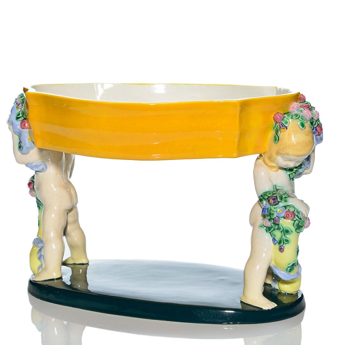 Wiener Kunstkeramische Werkstatte compote, putti 8x12: Wiener Kunstkeramische Werkstätte compote supported by polychromed putti at either end. Each putti holds a flower filled cornucopia and a garland of flowers around its head. Marked with the impre