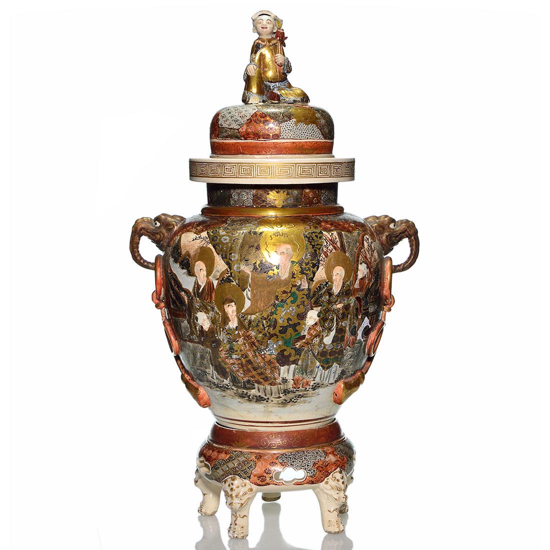 Satsuma Thousand Faces urn, cover, stand, 27 1/2”: Monumental Satsuma Thousand Faces covered urn on stand. Artist signed within the design. The urn with elephant head handles, their trunks grasping tasseled bows and decorated with Asian men outdoors o