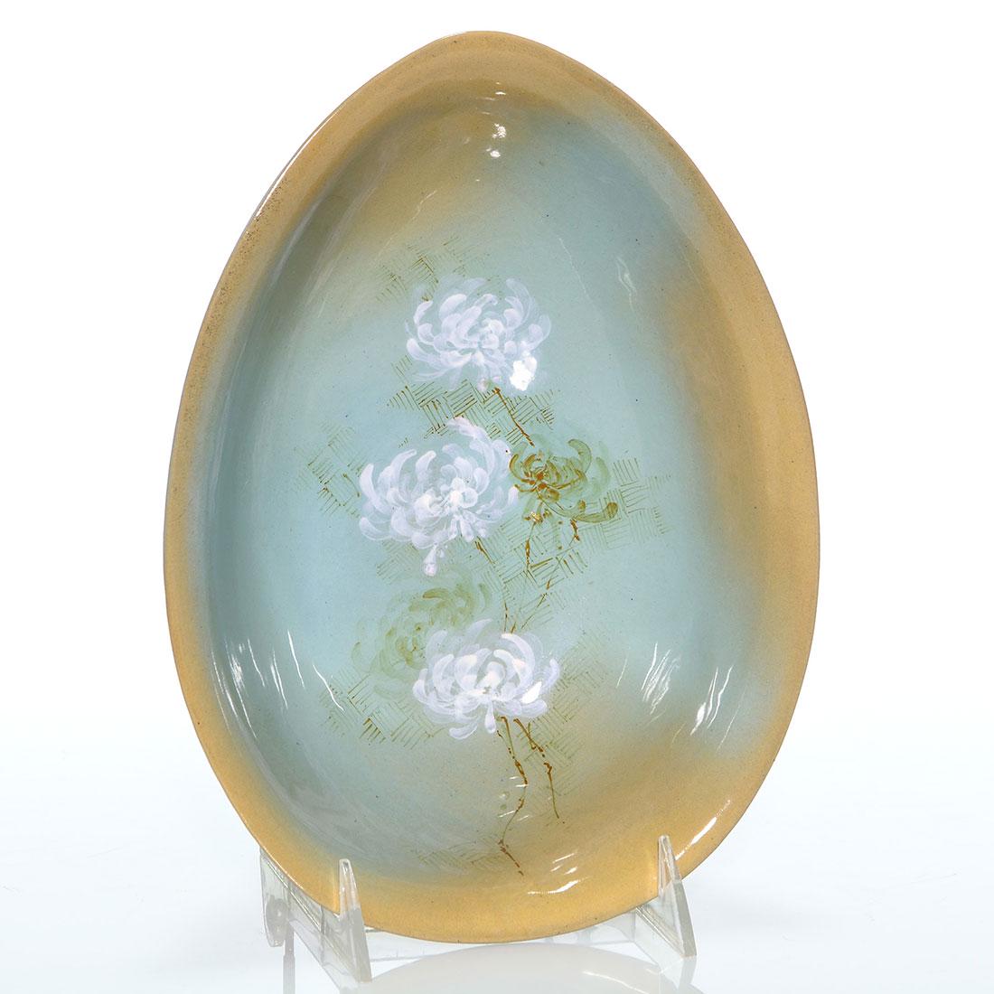 Rookwood Cameo bowl, Van Briggle, 1887, 3” x 10: Cameo glaze bowl shaped like an almond shell with two nub feet and decorated with white mums, the work of Artus Van Briggle in 1887. Marks include the Rookwood logo, which indicates the date, shape 31