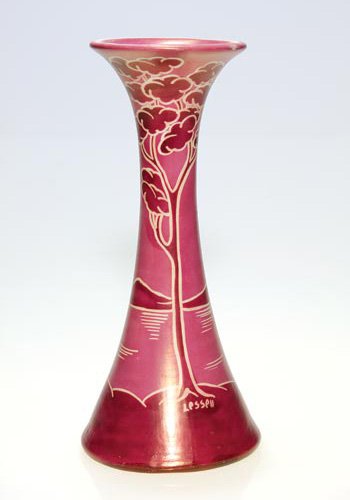 John Lessell luster scenic in red, 10": Luster vase decorated by John Lessell with a tropical scene depicting trees next to a bay with hills in the background, deployed in colors of red, pink and white. Signed Lessell on the side, otherwise