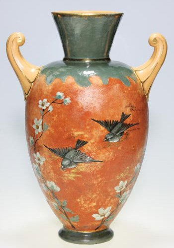 Matt Morgan vase, birds, Hirschfeld, 18 5/8": Matt Morgan Pottery Cincinnati Faience vase with two handles, depicting a pair of birds, one clutching a snack in its beak, flying amid some dogwood blossoms. There has been restoration to a chip at t