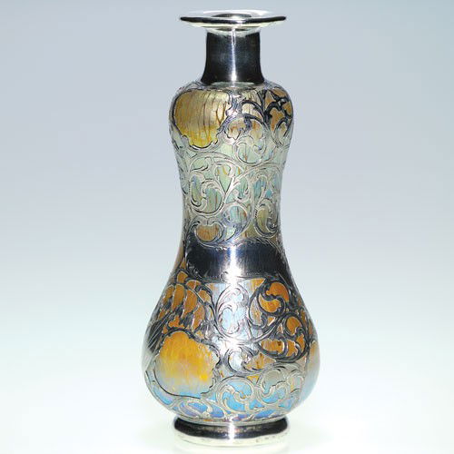 Loetz art glass vase with silver overlay, 7 1/8": Shapely Loetz vase enhanced with decorative silver overlay. The glass displays an overall Papillon pattern reflecting iridescent blue and gold. The silver has an intricate pattern showing stalks of li