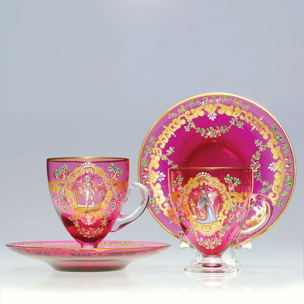Pr Moser attrib liqueur cups & saucers, enamel dec: Pair of liqueur cups and saucers attributed to Moser. The cranberry glass ornately enameled with 18 Century figures surrounded by colorful floral swags and golden scrolls. The footed cups measure 3 in