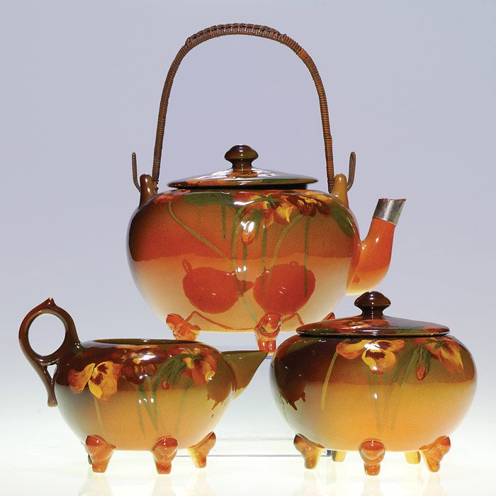 Rookwood Standard teaset, teapot, creamer, sugar: Standard Glaze tea set decorated with pansies by Carolyn Steinle in 1899. The 4 1/2 inch lidded teapot has a rattan handle. There are chips to the spout and the lid, which also bears the artist's mark