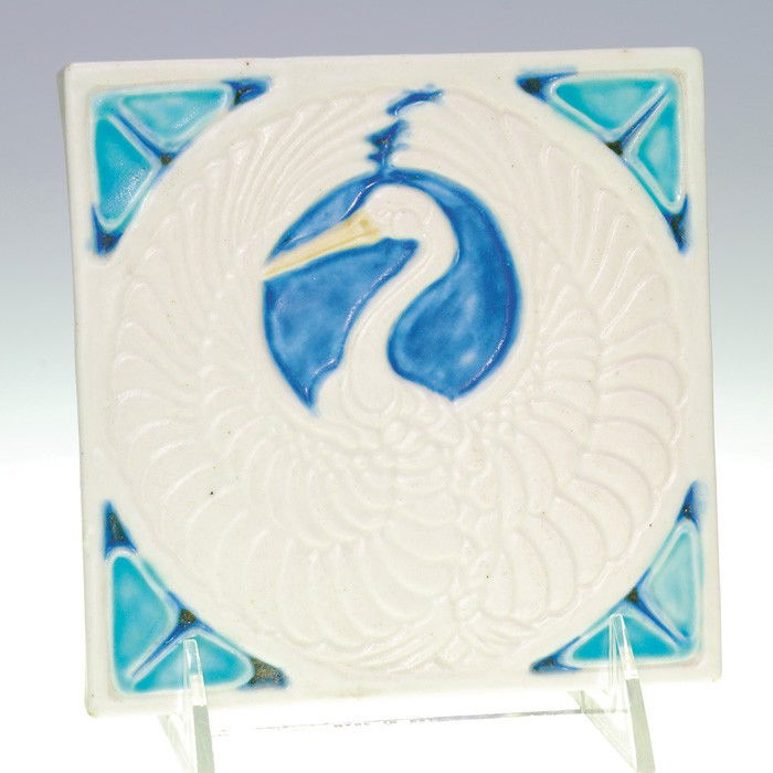 Rookwood mat trivet, stork, 1920, 2047, 5 1/2": Rookwood mat trivet showing a stork proudly strutting his white plumage and framed by turquoise "moth wings" in the corners and dark blue surrounding his head. Measures 5 1/2 inches square. Logo marks