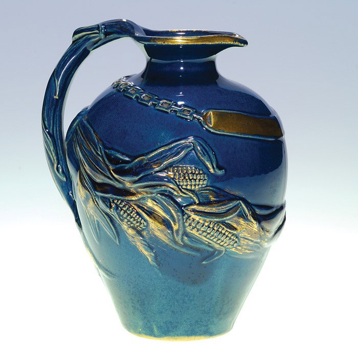 Matt Morgan jug, embossed corn, blue/gold, 6.75": Matt Morgan Pottery jug with corn and a nameplate on a chain, covered with a dark blue glaze and enhanced with much gilding. Impressed on bottom with the Matt Morgan logo and shape number 225. There i