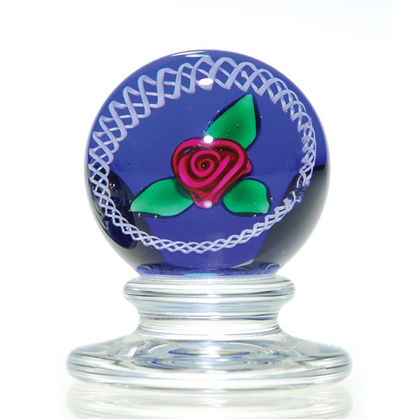 Mini Kaziun pedestal paperweight, ruby rose, 2": Miniature pedestal paperweight by Charles Kaziun Jr displaying a perfect ruby rose and green leaves enclosed by white filigree over a cobalt ground. Height 2 inches. Gold “K” embedded within. Perf