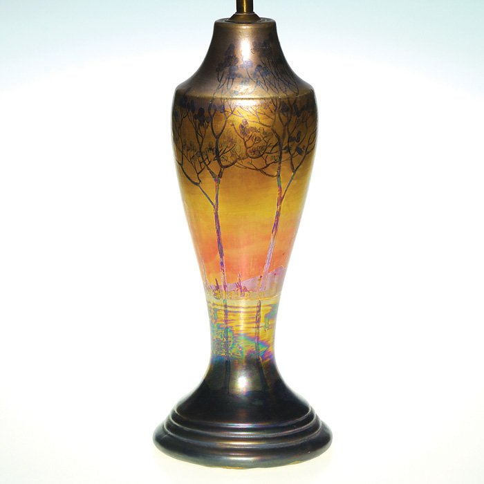 Weller or Camark 13 5/8” lamp vase, John Lessell: Weller or Camark original lamp decorated by John Lessell, who encircled the piece with a scene of trees bordering a lake with some hills in the background, arrayed in golden metallic luster colors. Un