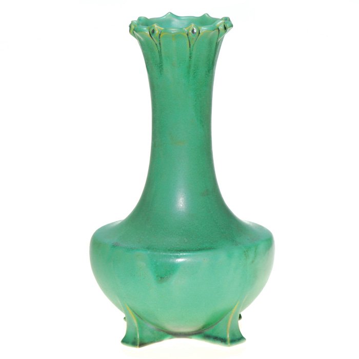 Teco 13” footed vase, floral design at rim.: Teco vase with molded design of lilies encircling the rim and having four feet, covered with the mat green glaze with charcoaling effect. Impressed twice with the Teco logo. There has been professiona