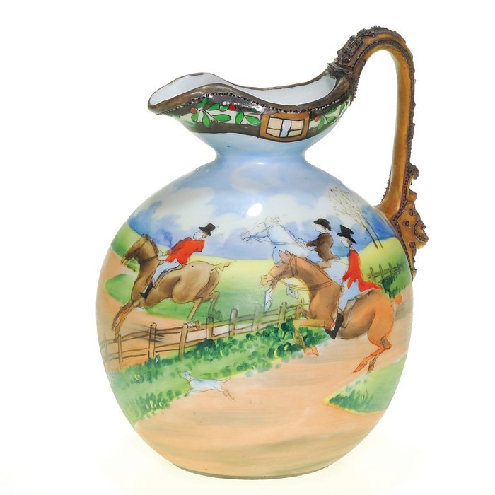 Nippon Morriage pitcher, Fox Hunters, 6 1/2”: Nippon Morriage pitcher with an English fox hunt theme showing horses with well attired ridders and hunting dogs scrambling across a fenced meadow. The handle is encrusted with decorative raised desig