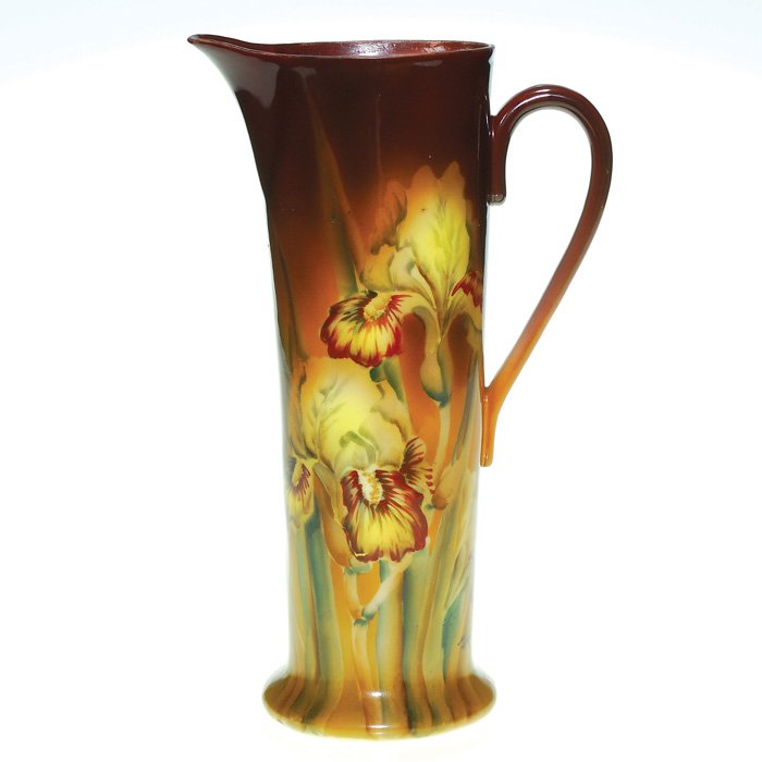 Nippon tankard, irises,10”, MK artist,maple leaf: Nippon tankard displaying a trio of yellow and brown irises framed by cocoa brown and mustard yellow. Height 10 inches. Artist MK monogram on the side. Green Maple leaf “Hand Painted Nippon” logo 