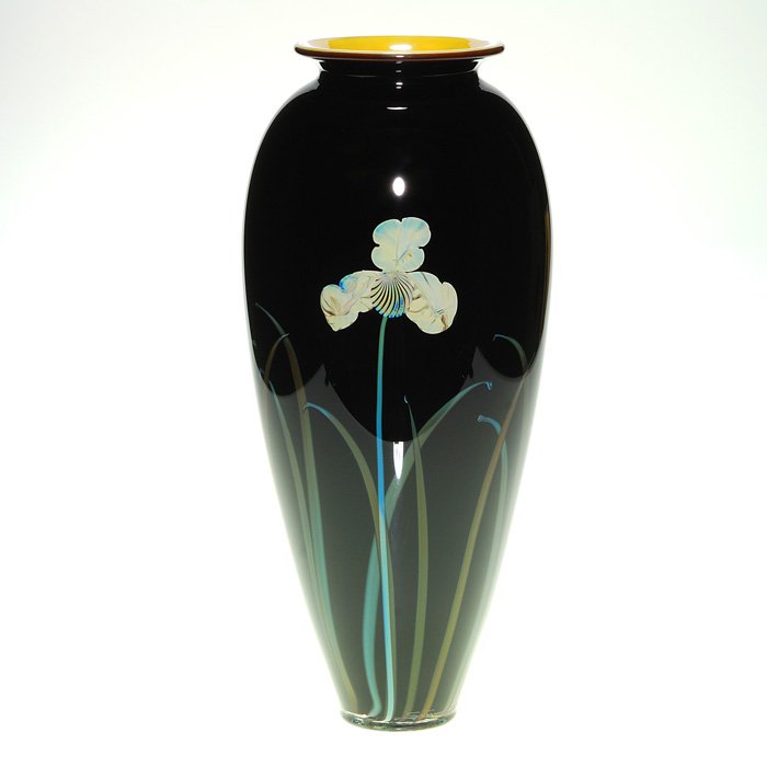 Satava pedestal vase, Irises, 13 3/4”, signed, 2004: Rick Satava “Three Iris” vase displaying ivory color flowers among slender bluish tan leaf blades arranged against an ebony backdrop. The flaring rim reveals a pretty tawny gold casing within. Hei