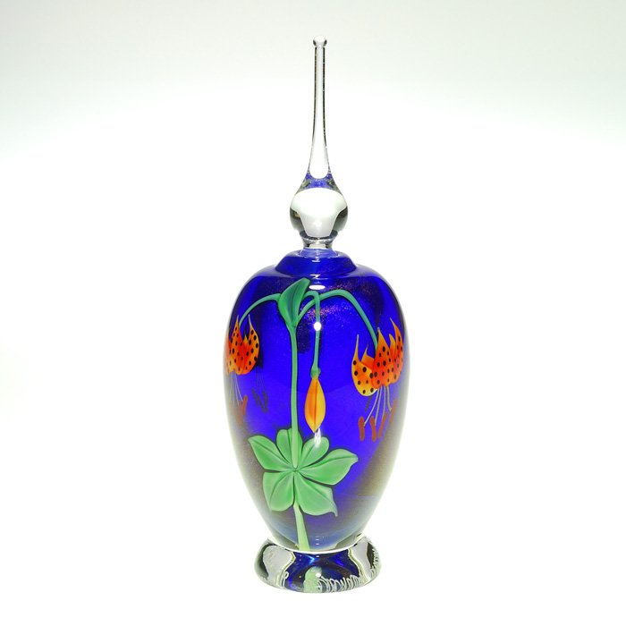 Orient & Flume perfume, stopper, Alexander, 8 1/2”: Orient & Flume perfume displaying a growth of orange tiger lilies brightly over a rich metallic cobalt backdrop created by Ed Alexander. A clear teardrop stopper with dauber adorns the top. The clear