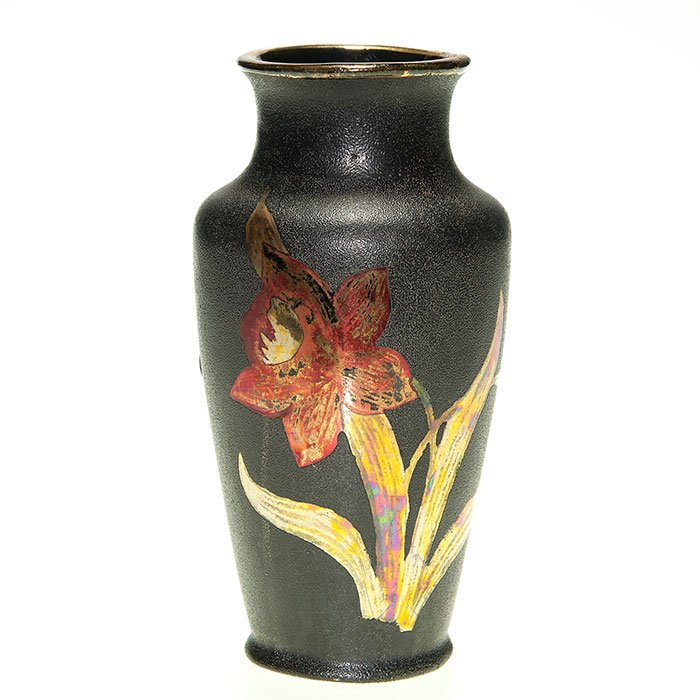 Camark vase, luster daffodil, ebony backdrop, 7 3/4”: Stylish Camark vase with a red and gold luster daffodil against an ebony leather-like backdrop possibly the work of John Lessell. Height 7 3/4 inches. Gold mark “Camark Pottery” beneath. A 3 inch