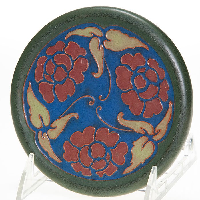 California Faience trivet, floral, 5 3/8”: California Faience 5 3/8 inch circular trivet with a repeating floral design, covered with dark green, light green, brown and blue mat glazes. Has the rectangular California Faience ink stamp on the b