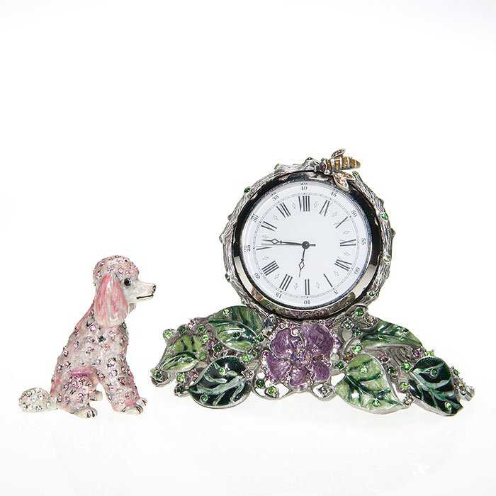 2 Jay Strongwater: signed desk clock; poodle figure: Two Jay Strongwater enamel, rhinestone and metal objects. First a 2 inch silvery pink poodle embedded with glittering rhinestones. Second an artist signed table clock mounted among leaves and wild ros