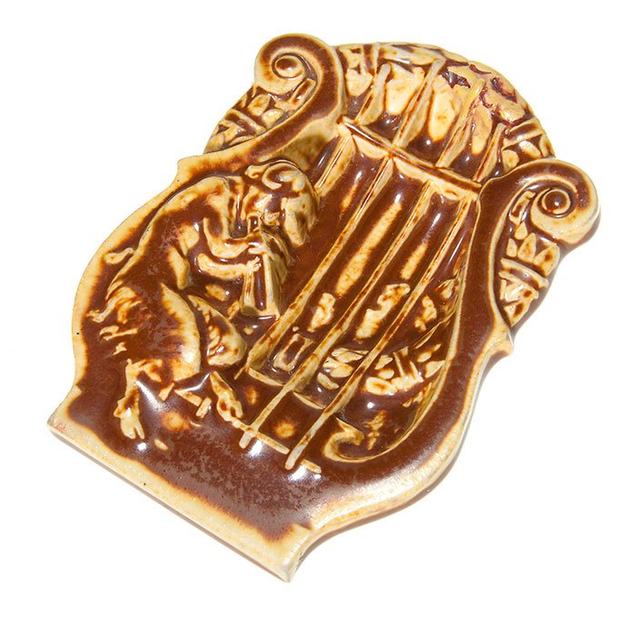Rookwood, pintray, Pan, 1927, 5 1/2”: Commercial ware plaque made for the 1927 convention of an organization with the initials NFWMC, depicting Pan seated on a harp while playing his syrinx. Marked on the reverse with the organization’s