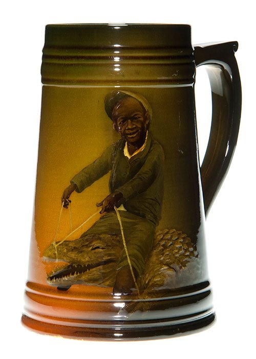Rookwood stein, Boy and Alligator, KS, 1896, 7”: Standard glaze mug with the image of a young black boy, dressed like a jockey, sitting astride an alligator with a riding crop in one hand and a rope connected to the gator’s nose in the other. Done