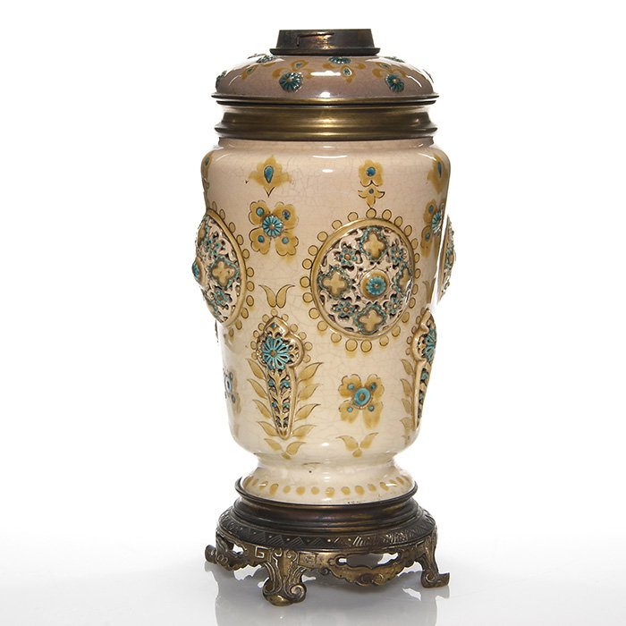 Early Zsolnay oil lamp with enameled top, 13 1/2”: Early Zsolnay oil lamp with brass font having a decorative enameled pottery shoulder. Reticulated medallions and cross symbols surround the body. Mounted on a metal base. Height 13 1/2 inches. Impress