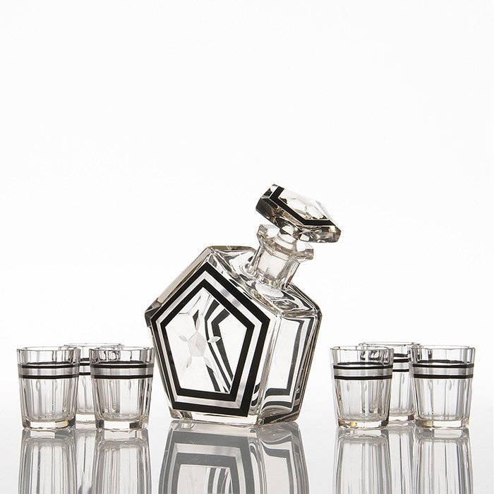 Art Deco cut decanter and 6 tumblers, 5 7/8”, 2 1/2”: Stylish Art Deco 5 7/8 inch pentagonal spirit decanter and stopper with six 2 1/2 inch tumblers. The set is cut and polished to perfection having wheel cut adornments and is handsomely trimmed in blac