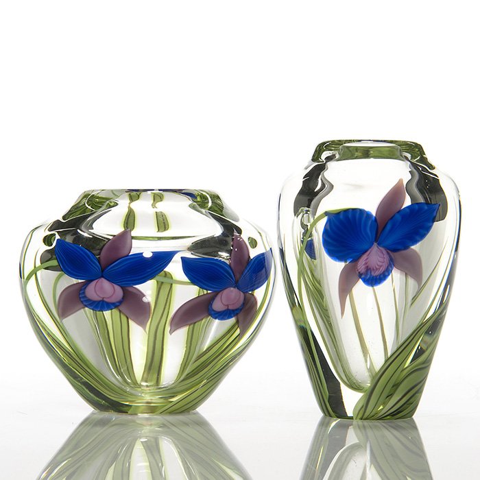 2 Orient & Flume vases, orchids, Held, 4” & 5”: Two signed Orient & Flume “reflective” vases displaying blue & mauve orchids and striped green leaves layered within. The 4 inch is signed by artist (Greg) Held with registration number. The 5 inc