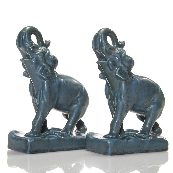 Pr Rookwood elephant bookends, trunks up, 7 1/8”: Pair of “Lucky” elephant bookends, having their trunks raised, cast in 1936 and covered with dark blue over lighter blue mat glazes. Marks include the Rookwood logo, date and shape 6124. Each also