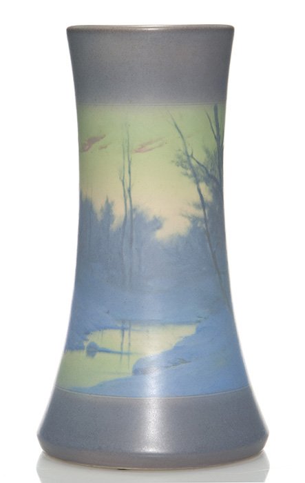 Rookwood Vellum scenic vase, Rothenbusch, 13 1/8”: Scenic Vellum vase decorated by Fred Rothenbusch in 1911 showing a winter scene with a stream between snow covered banks and stark trees. Marks include the Rookwood logo, date, shape 1358 B, an incise