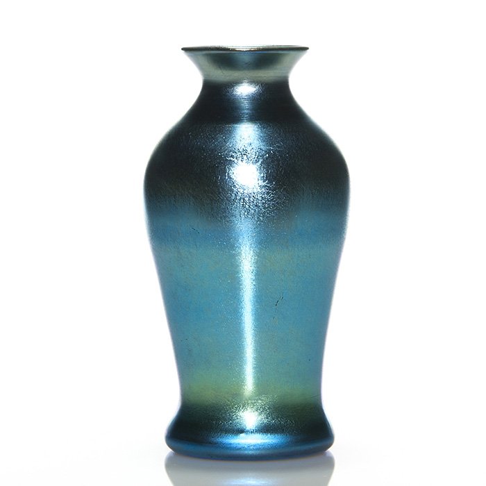 Quezal vase, iridescent blue, 8”, signed: Quezal vase rising 8 inches displaying a nice iridescent blue surface with a blush of gold here and there. Silver signed “Quezal” beneath. Minor short surface scratches. Pleasing color, simplistic