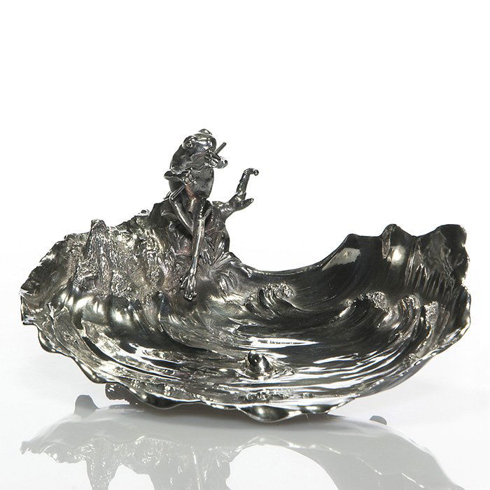 Silverplate dish, frog playing flute, fish, 3 1/4” X 9”: Whimsical silverplate figural tray of a bull frog seated at the edge of a pond, serenading to a curious fish who has come to the surface of the water, listening as the frog plays his flute. Height 3 1