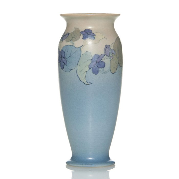 Rookwood vellum vase, violets, Rothenbusch, 6 1/8”: Vellum glaze vase nicely decorated with violets and leaves about the shoulder backed by tan and blue having a chocolate interior done by Fred Rothenbusch in 1930. Height 6 1/8 inches. The factory logo