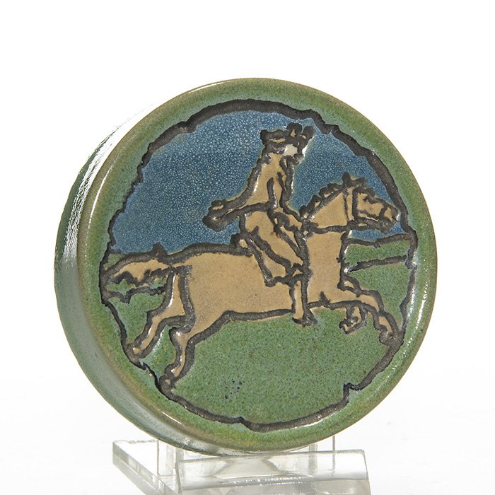 S.E.G. circular paperweight,Paul Revere,3 1/4” diam: Saturday Evening Girls paperweight depicting Paul Revere on horseback covered in blue, green and brown mat glazes. Marked on the bottom S.E.G. 6-14 and having the initials of artist Fannie Levine. In 