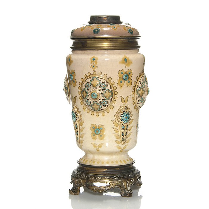 Early Zsolnay Oil Lamp with enameled top, 13 1/2”: Early Zsolnay oil lamp with brass font having a decorative enameled pottery shoulder. Reticulated medallions and cross symbols surround the body. Mounted on a metal base. Height 13 1/2 inches. Impress