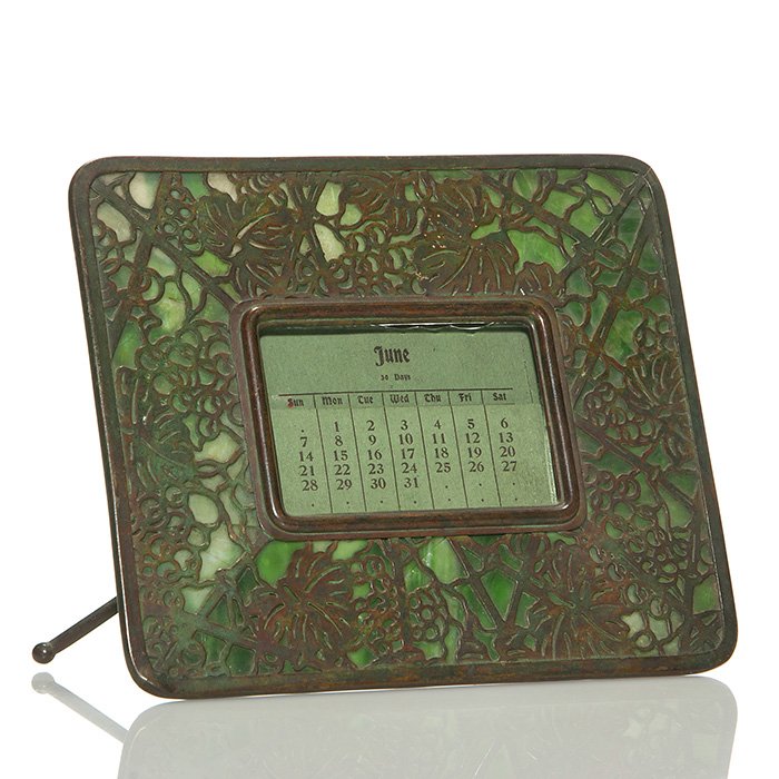 Tiffany Grape Leaf bronze easel calendar, 6”X7 1/8”: Bronze Tiffany “Grape Leaf” easel calendar frame with original perpetual paper calendar. Measures 6 inches by 7 1/8 inches across. Impressed “Tiffany Studios, New York, 940” on the back. The g