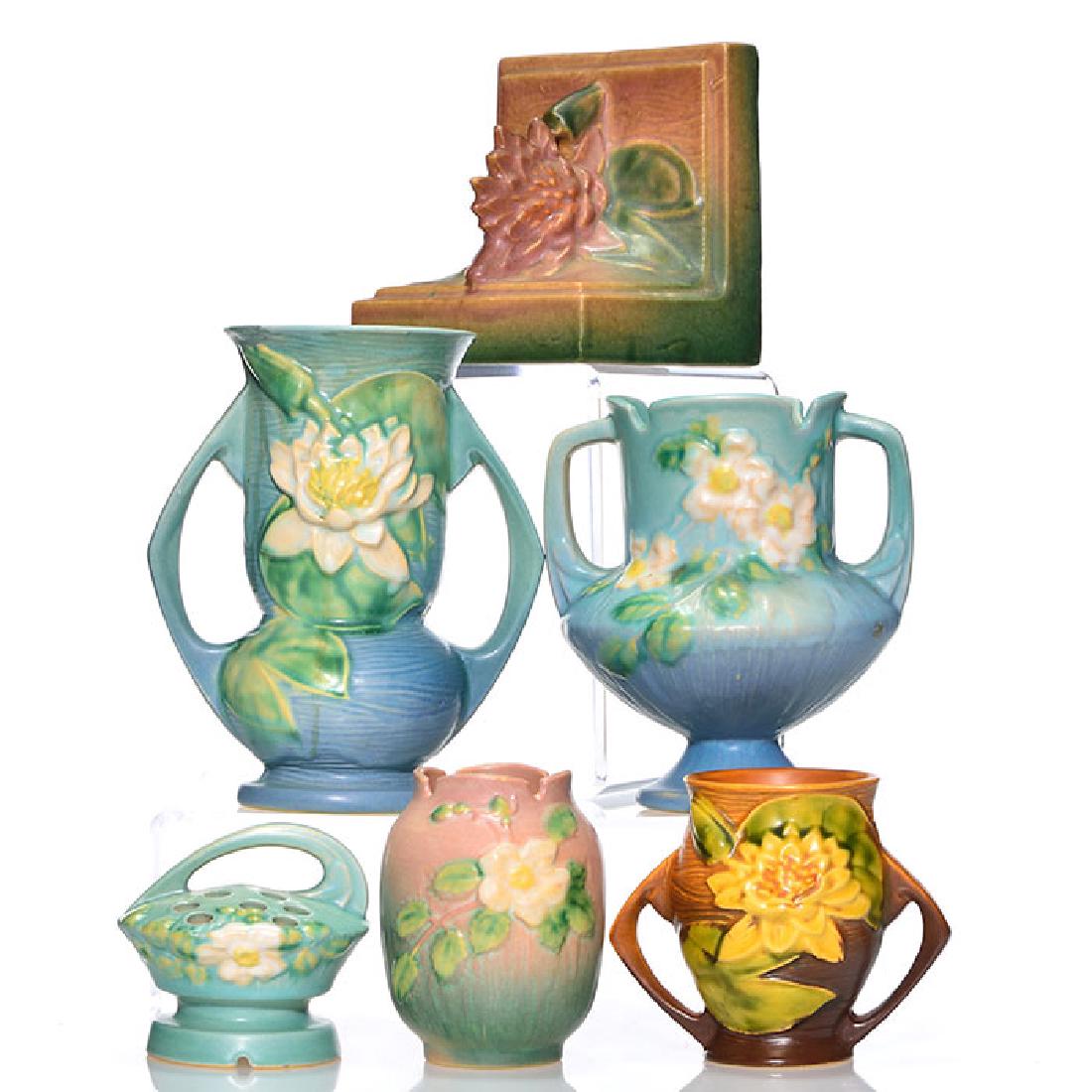 5 Roseville: 3 Water Lily, 3 White Rose: Five Roseville 3 Water Lily and 3 White Rose with raised marks. Water Lily consists a pink bookend, shape 12, 5 inches by 5 inches, tiny glaze nick to tip of flower, a blue vase, shape 74-7, 7 1/8 inc
