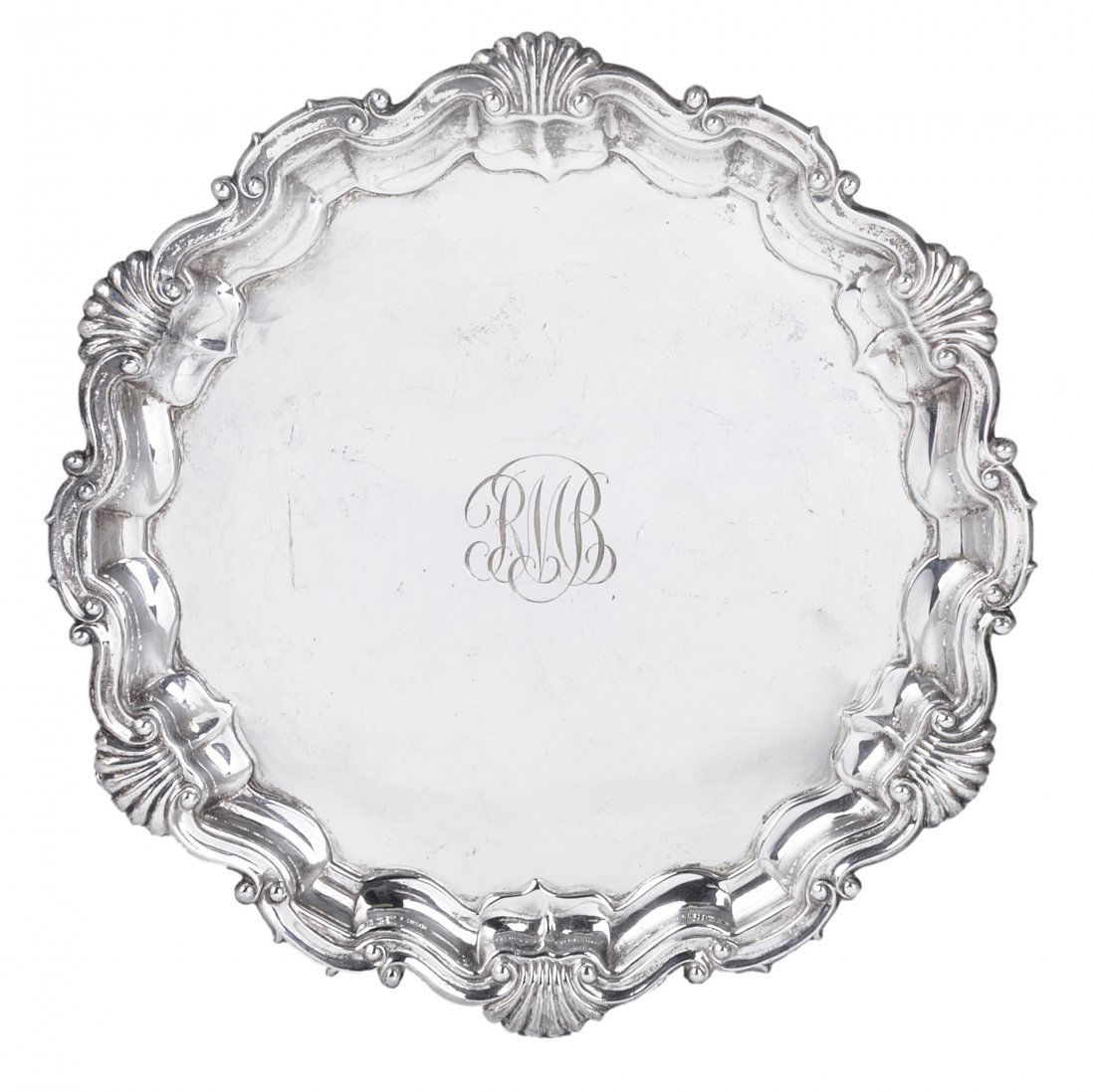 AN EDWARDIAN SILVER SALVER, THE GOLDSMITHS & SILVE: AN EDWARDIAN SILVER SALVER, THE GOLDSMITHS & SILVERSMITHS CO. LTD., LONDON, 1903 shaped circular, shell and scroll border, the centre engraved with the initials RMB, three claw and ball feet 21.7cm di