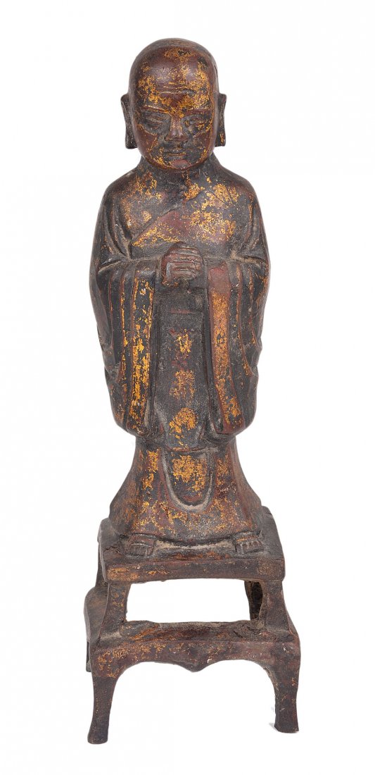 A CHINESE GILDED BRONZE FIGURE OF A MONK, MING DYNASTY: A CHINESE GILDED BRONZE FIGURE OF A MONK, MING DYNASTY (1368-1644) with traces of lacquer, modelled with hands clasped in prayer, on integral two-tier openwork stand 30.5cm high