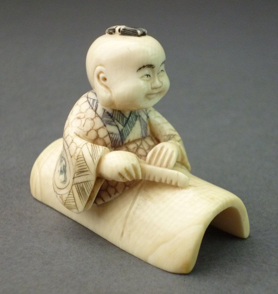 Netsuke, Knabe auf Bambusrohr, auf der Unterseite: Netsuke, Knabe auf Bambusrohr, auf der Unterseite versteckt sich ein kleiner Dämon, Mammutelfenbein, Ritzornametik farbig gefasst, seitlich mit Signatur, Doppelbohrung gut erhalten, L= 4,0cm, H= 