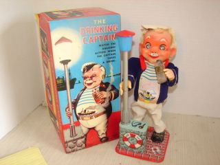 Drinking Captain Battery Operated Toy: The Drinking Captain holding a bottle of Old Hooch has a pack of Lucky Strikes laying by his feet on the Tin litho base he stands on. Box says he emits smoke when he drinks . Very good condition. Box