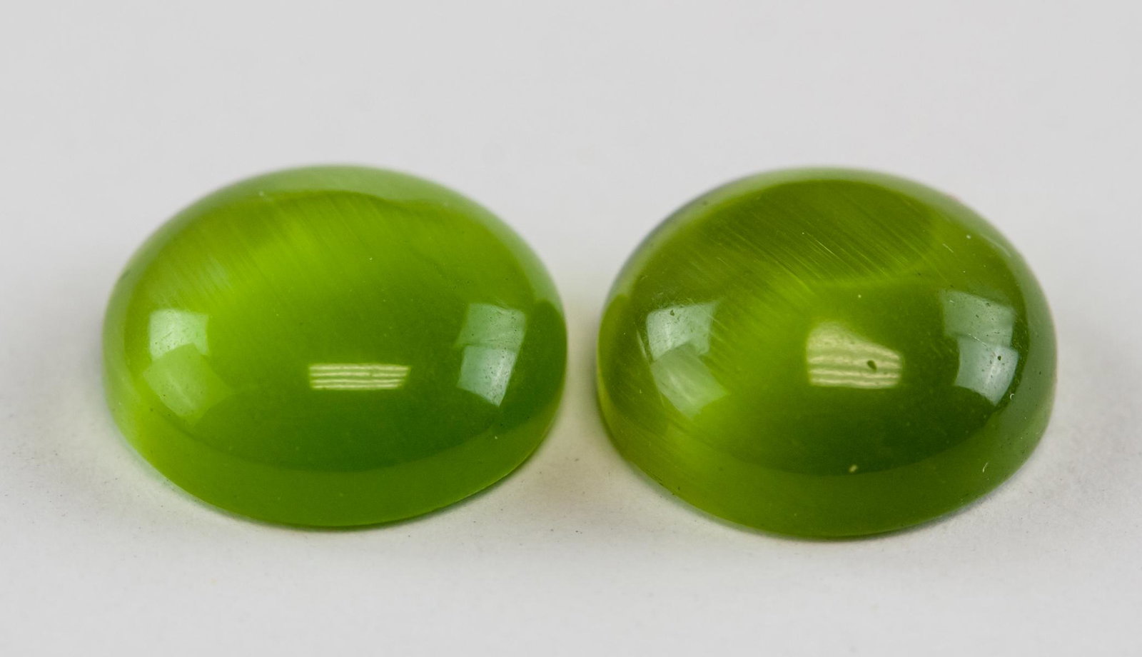 12.16ct Cabochon Cut Green Cats Eye Gemstone Pair: Two (2) 12.16ct (total) cabochon cut green cats eye gemstones. Diameter:12mm