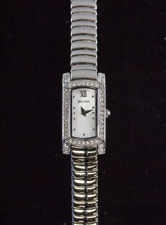Women's Watch Bulova: Women's watch. "BULOVA" on rectangular watch face. Set with clear gemstones around watch face. With silver-colored band. "BULOVA / B5 STAINLESS STEEL 96L207 / WATER RESISTANT / C8331146 / 17566237" on