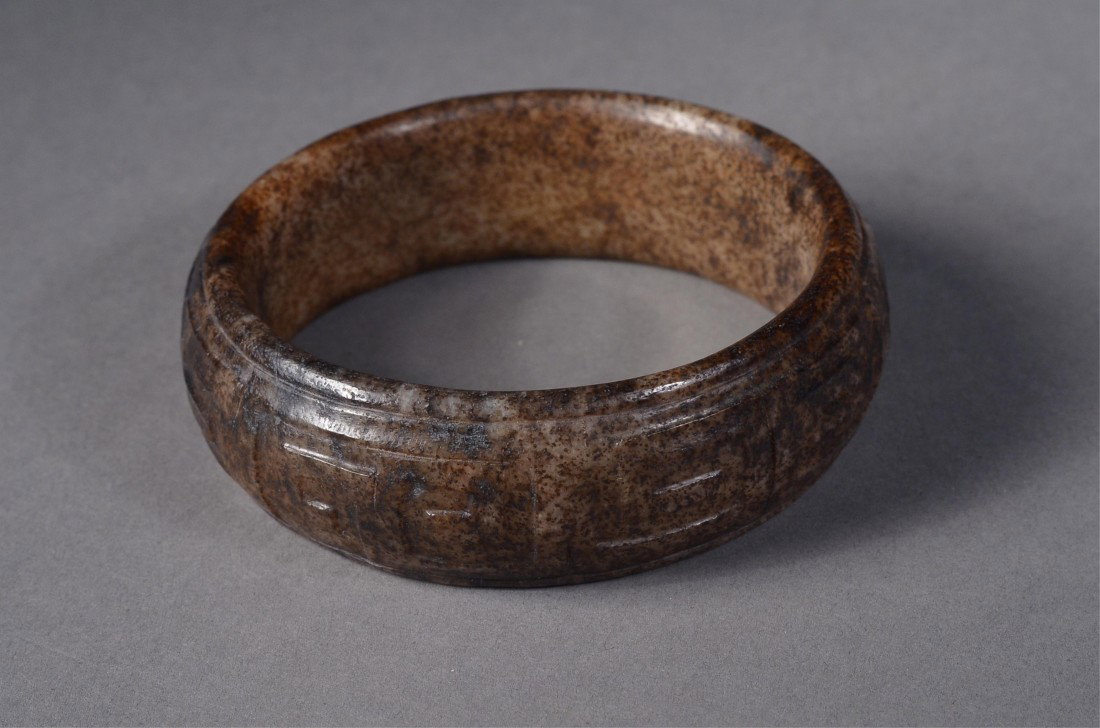 Chinese White Jade Bangle Key-Fret Band & Dragon: Chinese carved jade bangle; featuring key-fret relief carvings and geometric dragons chasing pearl; dark suffusions throughout; D: 8.5 cm 107 grams