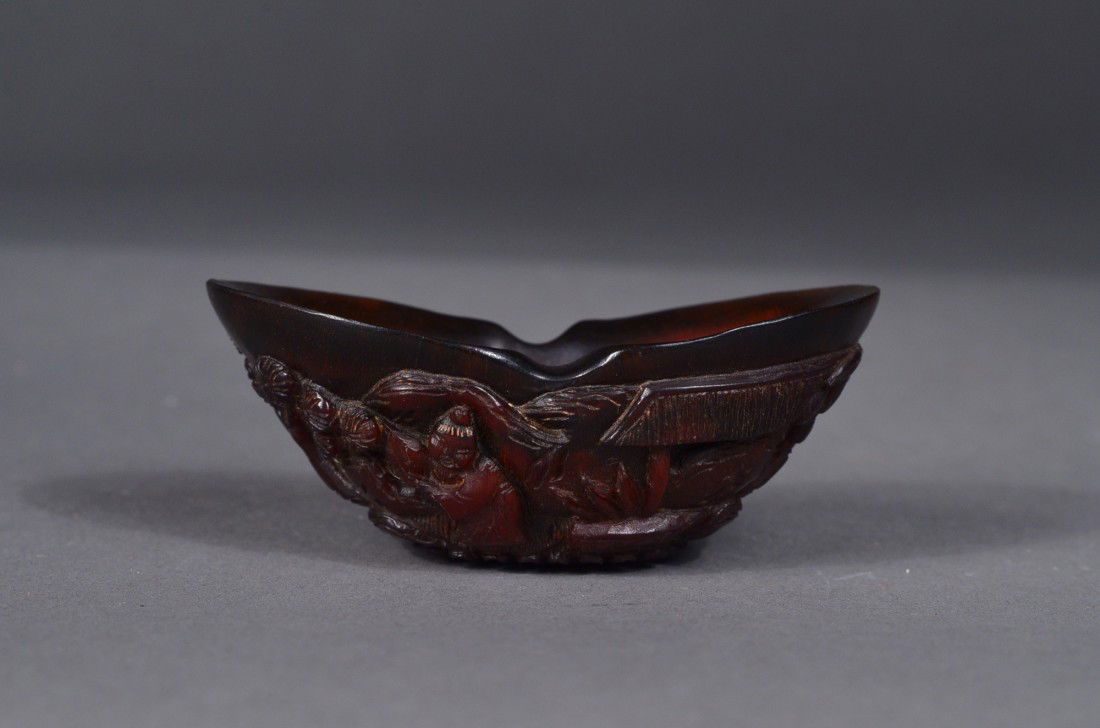 Chinese Rhinoceros Horn Carved Cup: Well carved Chinese rhinoceros horn cup; of compressed form: featuring carving throughout exterior in relief, raised upon a circular foot with lappet border; L: 7 cm, H: 3 cm
