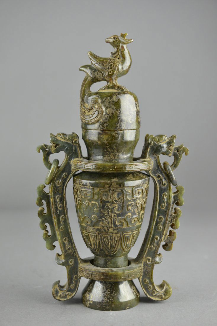 Archaistic Chinese Carved Spinach Green Jade Vase: Archaistic Chinese carved jade vase; a sectional ovoid body with tapering body featuring archaistic geometrically-shaped dragons in relief; handles in form of lion heads; domed cover surmounted by pho