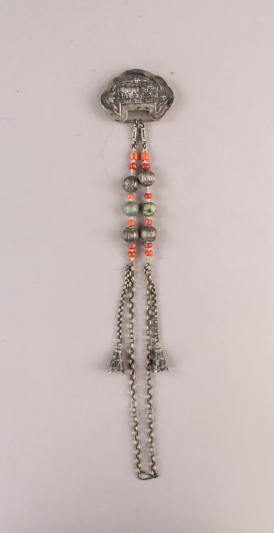 Chinese Tibetan Silver Carved Necklace: The pendant is connected to a string of beads and silver elements, creating a harmonious blend of textures and colors. Red and green beads intersperse with silver adornments, leading down to two disti