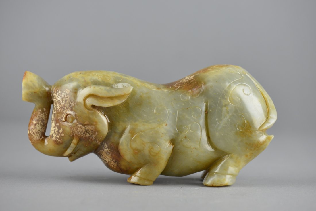 Archaistic Chinese Carved Jade Figure of Elephant: Archaistic Chinese carved jade figure; featuring elephant in recumbent pose; the stone of translucent dark celadon tone with mutton fat suffusions; L: 19.5 cm, H: 9.5 cm, W: 6 cm, 1348 grams