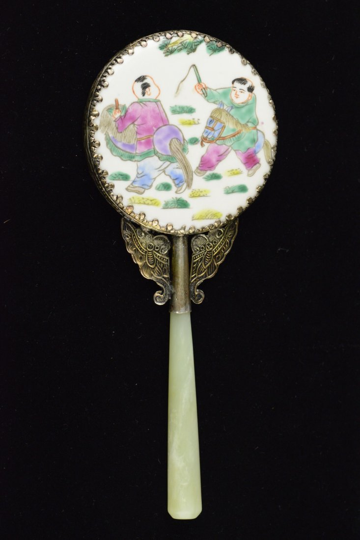 A Chinese Hand Mirror with Jade Handle: Chinese hand mirror, featuring a round porcelain plaque painted children at play. Handle flanked with pair of bronze butterflies with white jade handle. D: 8 cm, L: 20 cm, 146 grams.